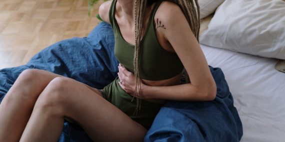 Woman sitting in bed holding her stomach, indicating pain or discomfort, possibly due to cramps.